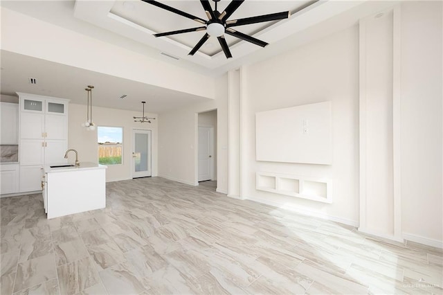 unfurnished living room with ceiling fan with notable chandelier, a raised ceiling, and sink