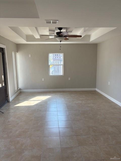 empty room with light tile patterned flooring, ceiling fan, and a raised ceiling