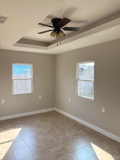 empty room with a raised ceiling, light tile patterned flooring, and ceiling fan