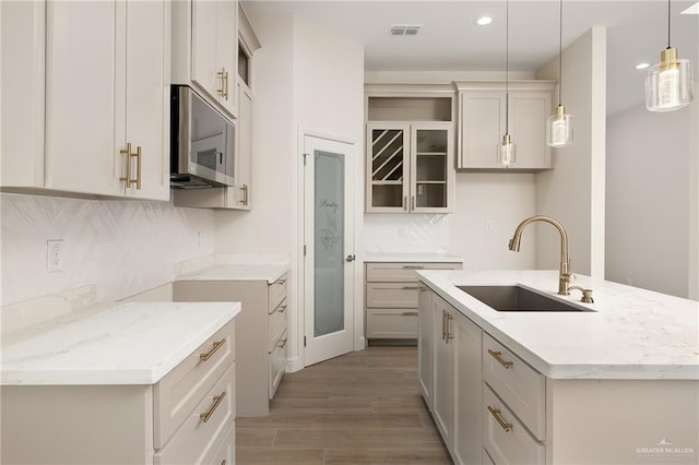 4909 Columbia Ave, Mcallen, TX 78504 - kitchen with a sink, stainless steel microwave, light stone countertops, a center island with sink, and decorative backsplash