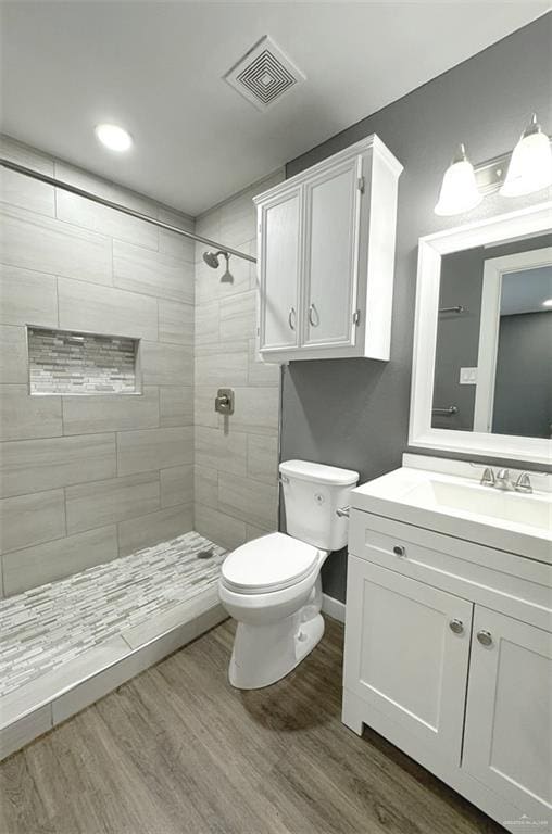 bathroom featuring hardwood / wood-style flooring, vanity, toilet, and tiled shower