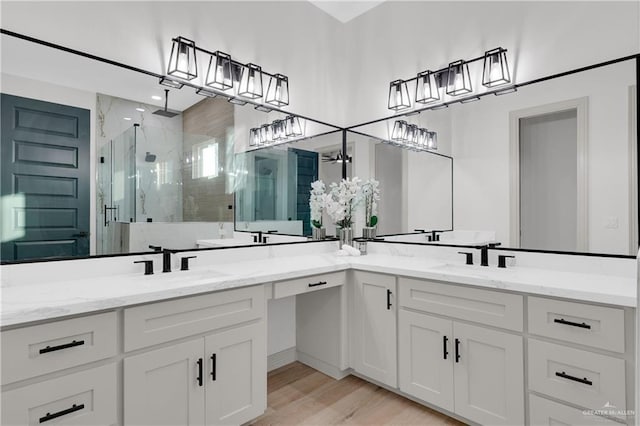 bathroom with double vanity, a shower stall, a sink, and wood finished floors