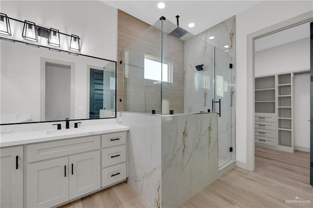 bathroom featuring a spacious closet, vanity, a marble finish shower, and wood finished floors