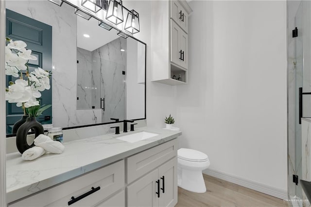 bathroom featuring a marble finish shower, toilet, vanity, wood finished floors, and baseboards