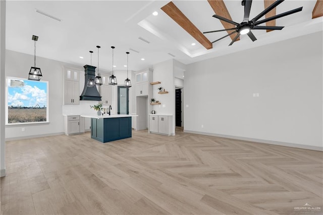 kitchen featuring custom range hood, baseboards, open floor plan, and a center island with sink