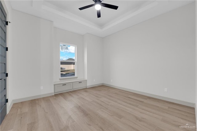 unfurnished room with light wood finished floors, ceiling fan, baseboards, and a raised ceiling