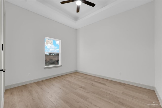 spare room featuring a ceiling fan, a raised ceiling, baseboards, and light wood finished floors