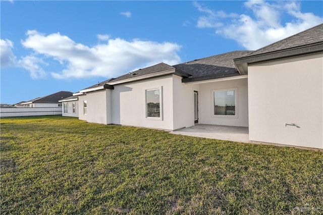 rear view of house featuring a yard, a patio, fence, and stucco siding