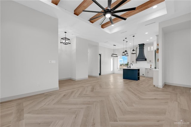 unfurnished living room with ceiling fan with notable chandelier, a tray ceiling, baseboards, and recessed lighting