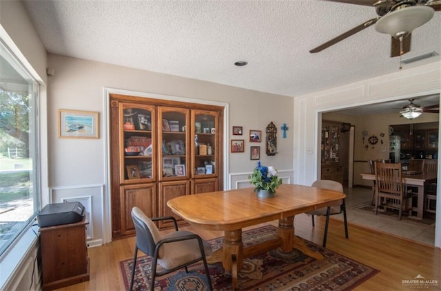 2517 E Mile 4th Rd, Mission, TX 78573 - dining space featuring a ceiling fan, a decorative wall, a textured ceiling, light wood-style flooring, and wainscoting