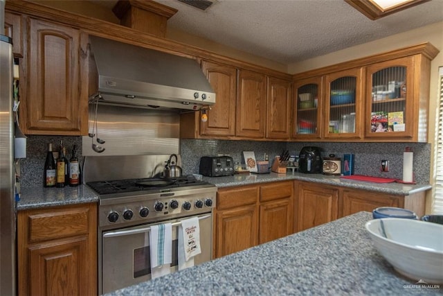 2517 E Mile 4th Rd, Mission, TX 78573 - kitchen featuring stainless steel appliances, wall chimney range hood, brown cabinetry, glass insert cabinets, and decorative backsplash