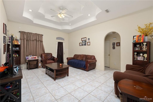 living room with ceiling fan, light tile patterned flooring, and a tray ceiling