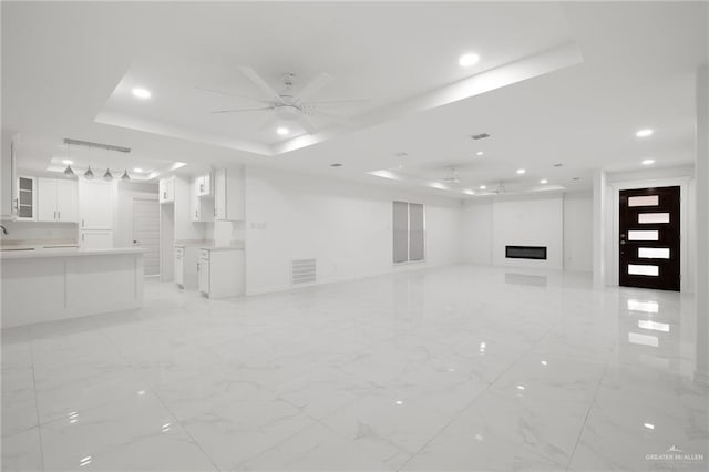 unfurnished living room with a fireplace, a raised ceiling, and ceiling fan