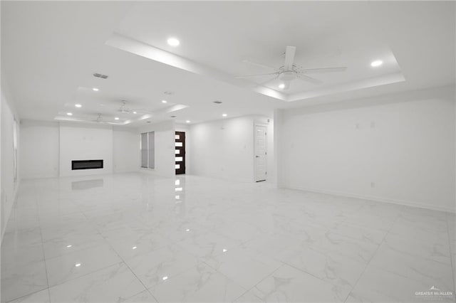 unfurnished living room featuring a raised ceiling and ceiling fan