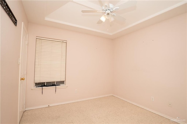 empty room with ceiling fan and a raised ceiling