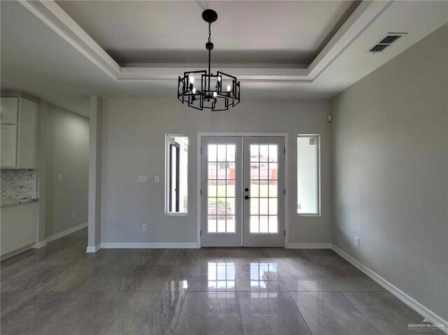 doorway to outside featuring french doors, an inviting chandelier, and a raised ceiling