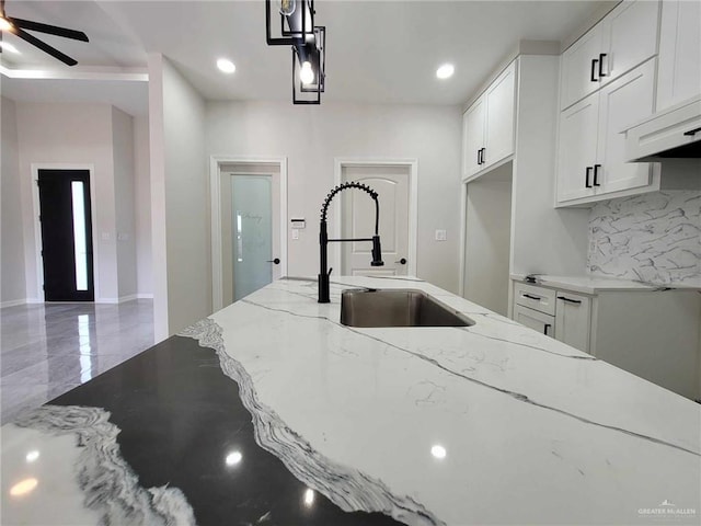 kitchen with tasteful backsplash, light stone counters, sink, and white cabinetry