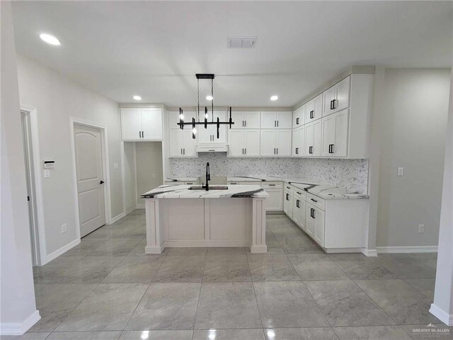 kitchen featuring hanging light fixtures, a kitchen island with sink, sink, and light stone counters