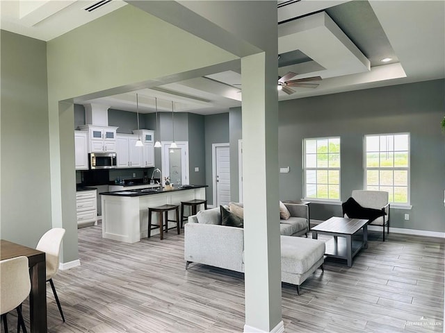 living area featuring light wood finished floors, baseboards, visible vents, ceiling fan, and a high ceiling