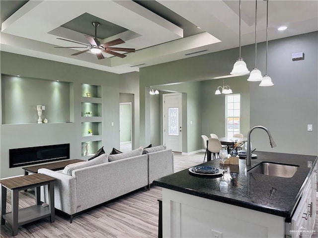 living room featuring visible vents, a raised ceiling, light wood-style floors, built in shelves, and a fireplace