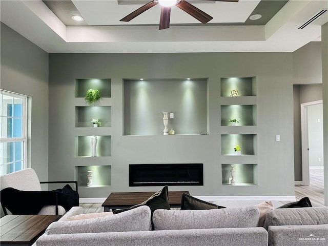 living room with built in shelves, a glass covered fireplace, a raised ceiling, and visible vents