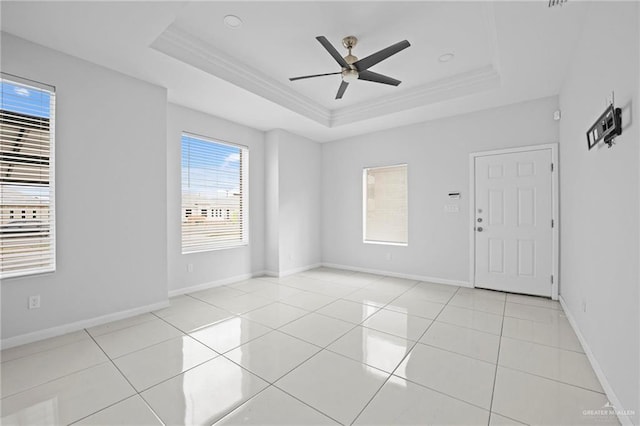 empty room with light tile patterned flooring, ceiling fan, crown molding, and a raised ceiling