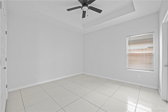 tiled empty room featuring a raised ceiling and ceiling fan