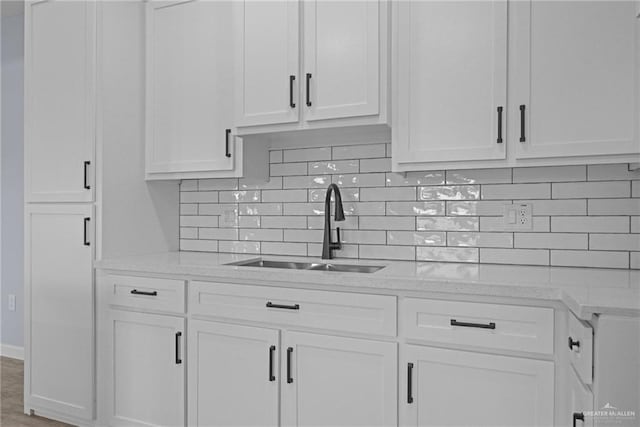 kitchen with light stone counters, sink, decorative backsplash, and white cabinets