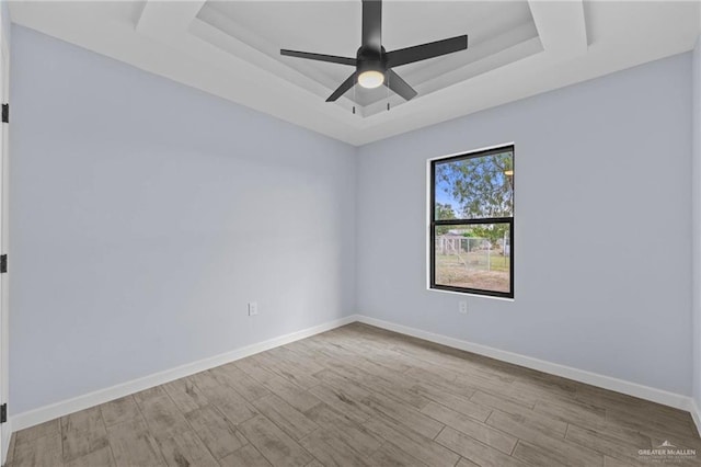 empty room featuring ceiling fan, a tray ceiling, and light hardwood / wood-style floors