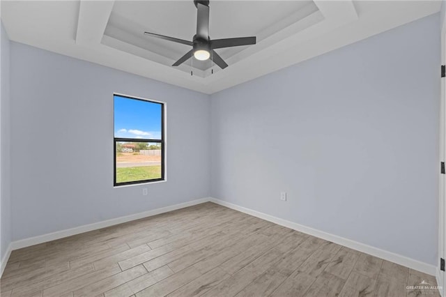 empty room with light hardwood / wood-style flooring, ceiling fan, and a tray ceiling