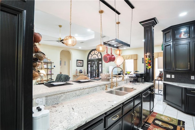 kitchen featuring a tray ceiling, pendant lighting, light tile patterned floors, a sink, and dark cabinetry