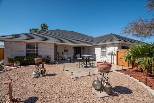 back of property with a tile roof, brick siding, and fence