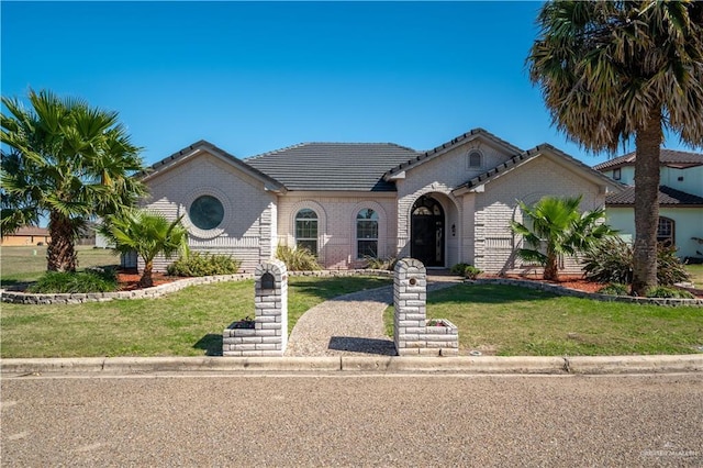 view of front facade with a front yard, brick siding, and a tiled roof