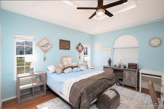 bedroom featuring ceiling fan, a tray ceiling, light wood-style flooring, and baseboards