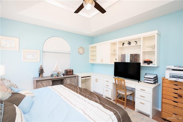 bedroom featuring ceiling fan, a tray ceiling, built in desk, and light wood-style flooring