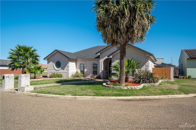 view of front of house with a tile roof, fence, a front lawn, and brick siding