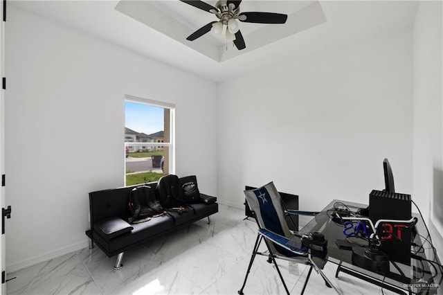 office featuring a raised ceiling, ceiling fan, marble finish floor, and baseboards