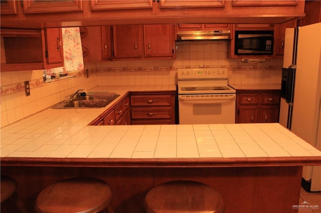 kitchen featuring tile counters, sink, kitchen peninsula, white appliances, and a kitchen bar