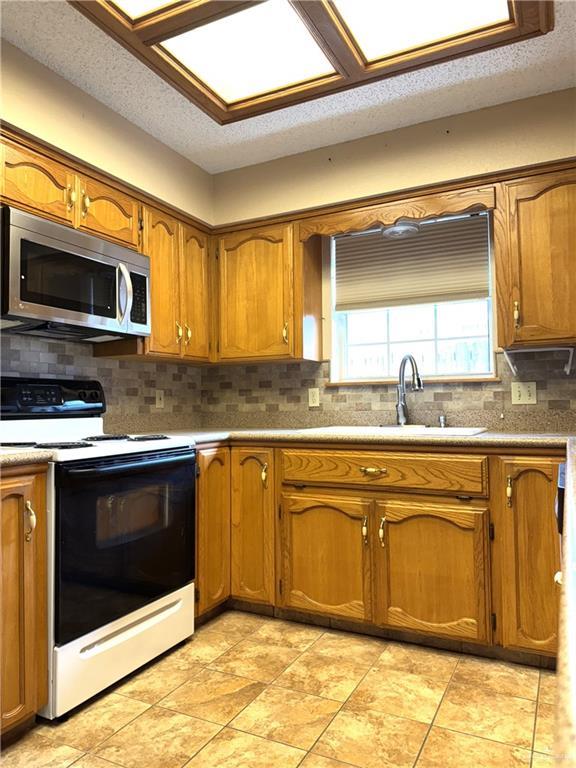 kitchen featuring brown cabinetry, electric range, a sink, stainless steel microwave, and backsplash