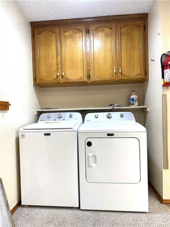 washroom with washer and clothes dryer, cabinet space, a textured ceiling, and baseboards