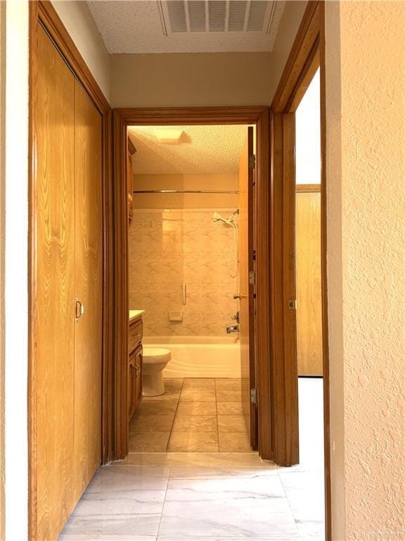 corridor with light tile patterned flooring, visible vents, a textured ceiling, and a textured wall