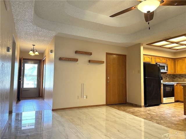 kitchen featuring stainless steel microwave, range with electric cooktop, brown cabinets, freestanding refrigerator, and a raised ceiling