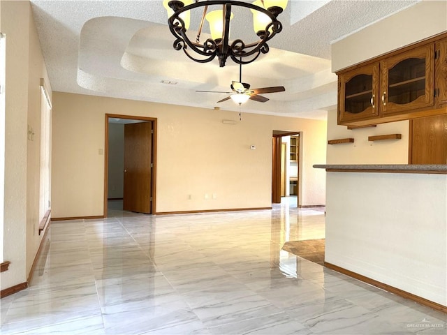 empty room with baseboards, a tray ceiling, ceiling fan with notable chandelier, marble finish floor, and a textured ceiling