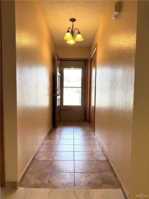 doorway to outside featuring tile patterned floors, a textured ceiling, baseboards, a chandelier, and a textured wall