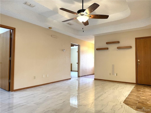 empty room with a tray ceiling, baseboards, visible vents, and a textured ceiling