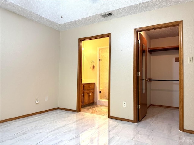 unfurnished bedroom with a closet, a textured ceiling, a walk in closet, and baseboards