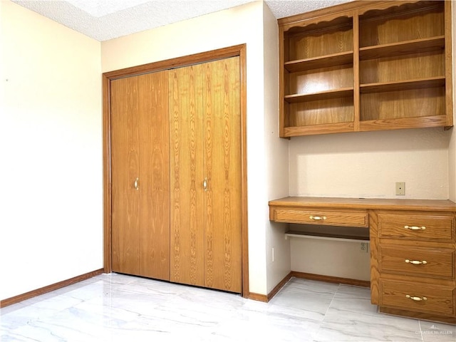 unfurnished office with baseboards, built in desk, marble finish floor, and a textured ceiling