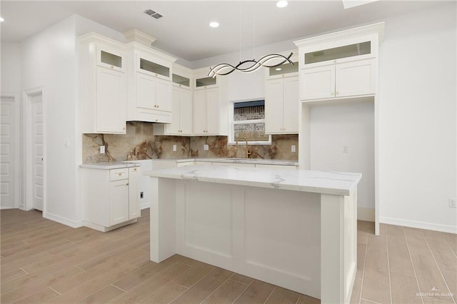 kitchen with light stone counters, white cabinetry, a center island, and sink