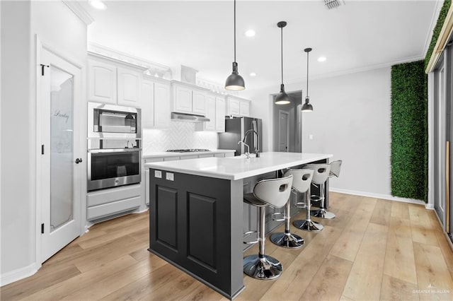 kitchen with white cabinetry, a center island with sink, appliances with stainless steel finishes, decorative backsplash, and hanging light fixtures