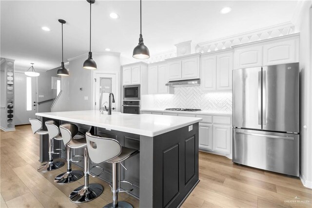 kitchen featuring tasteful backsplash, hanging light fixtures, a kitchen island with sink, stainless steel appliances, and white cabinets